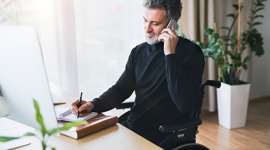 Un homme écrit dans un cahier tout en parlant au téléphone et se demande s’il doit présenter une réclamation habitation.