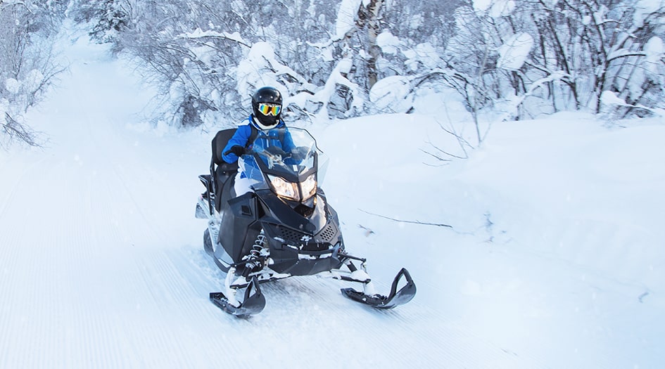 An individual rides a snowmobile on a snowy trail, following essential safety tip for snowmobilers