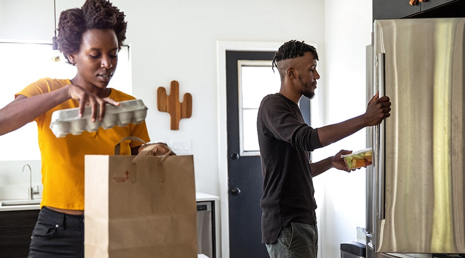 Two individuals unload groceries in their kitchen, as they think about the right tenant insurance limits for their rental