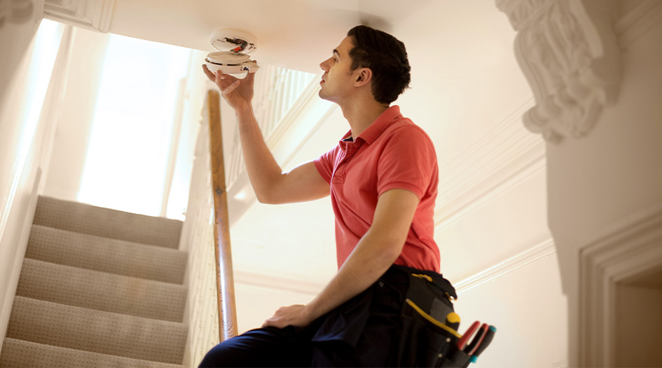 A man installs a smoke detector on the ceiling showing one way to prevent fires at home