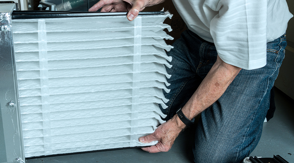 A close-up on a man installing a new furnace filter shows one regular home maintenance task every homeowner should know