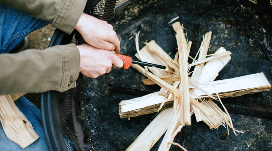 A close up on a person lighting kindling in a firepit shows one safety tip for backyard bonfires