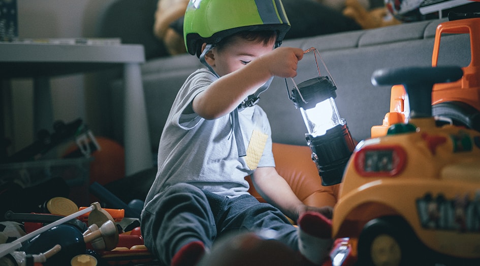 A child plays with a flashlight while sitting on the floor, showing how you should prepare for a summer power outage