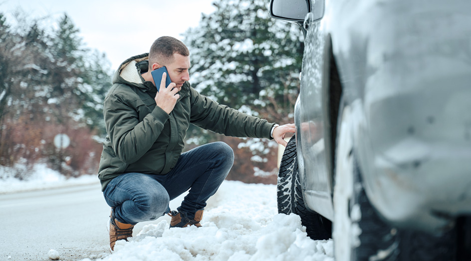 A man kneels beside his car while talking on his cellphone, showing what to do if you’re in an accident with a rental car