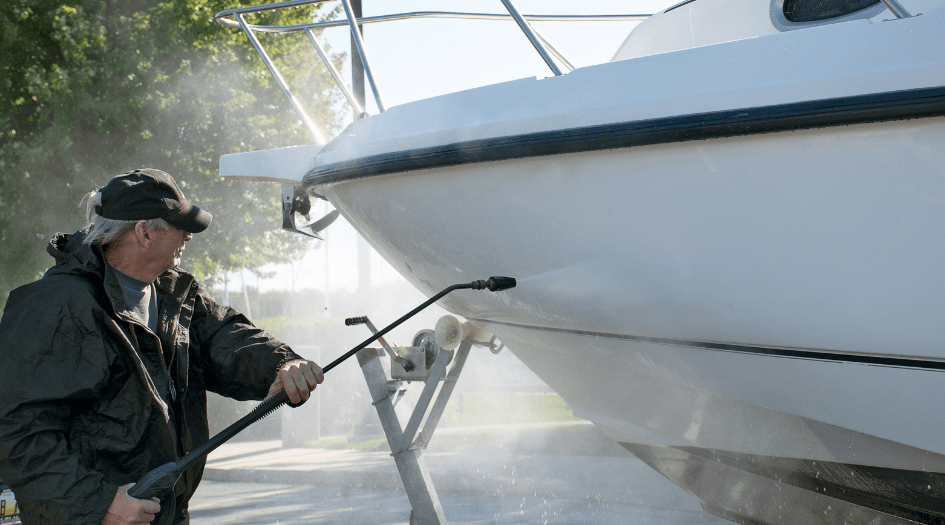 A man sprays down the hull of his boat with a pressure washer, showing one necessary step on how to winterize your boat.