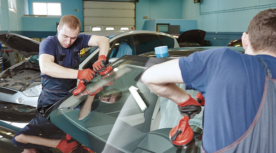Two men replace a windshield on a car, showing you one way to deal with a chipped or cracked windshield
