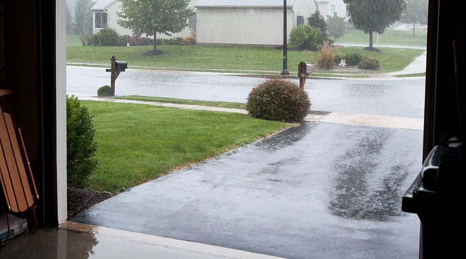 Heavy rain falls onto a driveway, showing why you should be aware of tips to prevent flood damage in your home