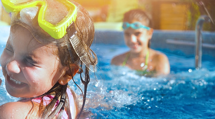 Two kids play in the pool with goggles on, showing a water safety tip for the summer