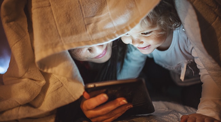 A woman and child look at a mobile phone under a blanket, as they research what to do before, during, and after a winter power outage