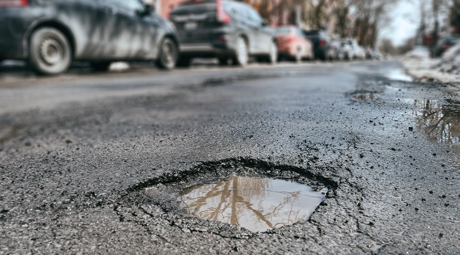 Here's what to do if your car is damaged by a pothole, as shown by a close up of a pothole filled with water