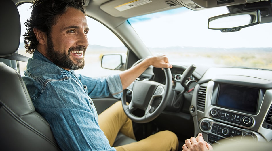 A man smiles behind the wheel of his car as he finds 10 ways to save on car insurance