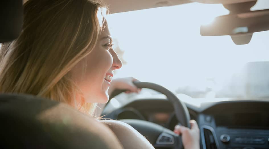 A girl smiles while sitting in the driver seat of a car, showing what you should know before buying car insurance for your teen