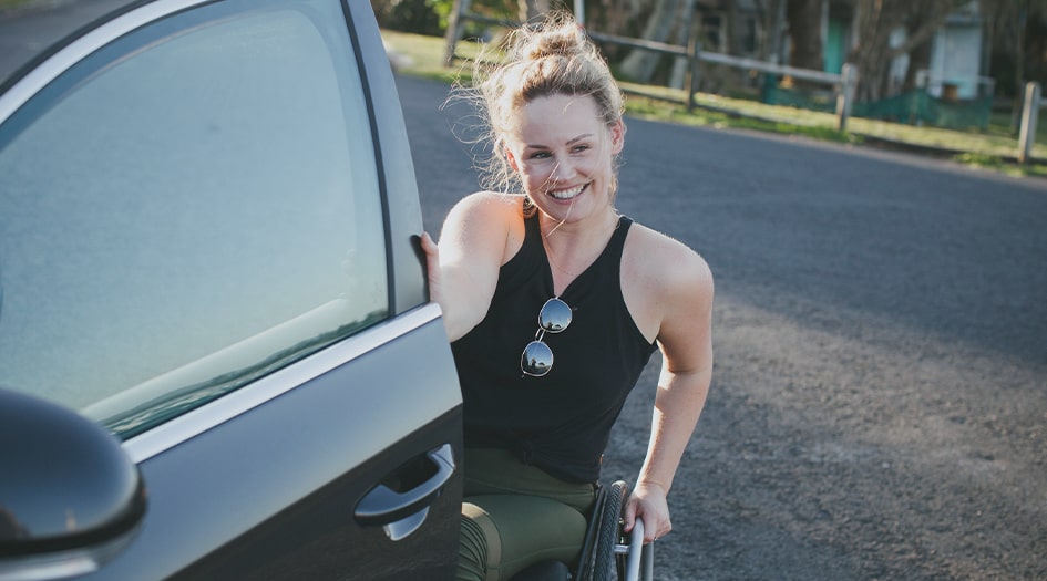 A woman in a wheelchair opens her car door, showing how vehicle modifications affect car insurance