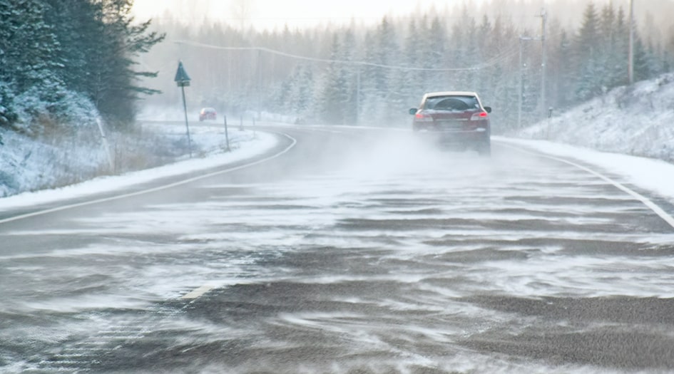 There are 10 items to keep in a winter driving emergency kit, as shown by a car driving down a snowy road