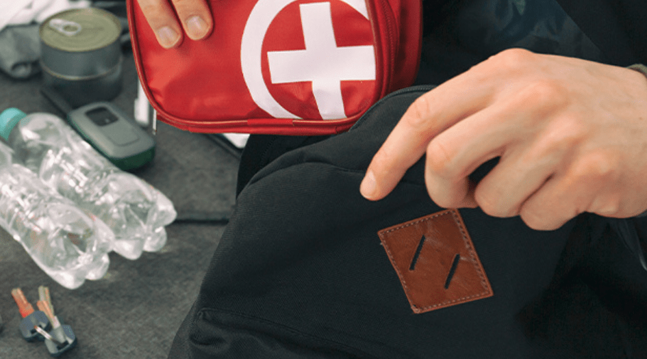 A man packs a first-aid kit, water bottles, and a walkie talkie into a backpack, showing what to do before an evacuation.