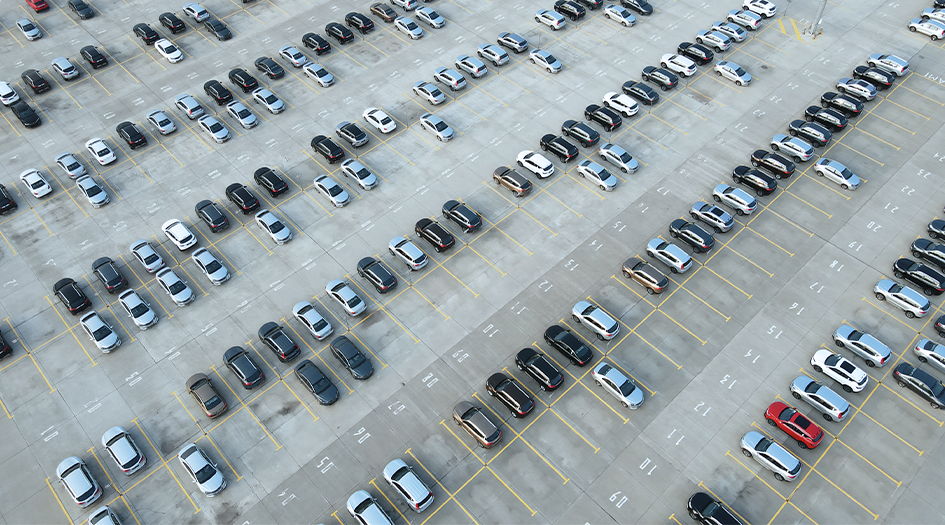 An aerial shot of a parking lot full of cars shows how supply chain disruptions are affecting car insurance claims