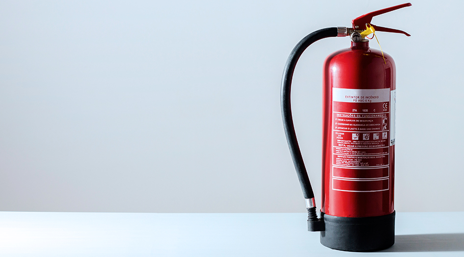 A red household fire extinguisher stands alone on a white table in a white room