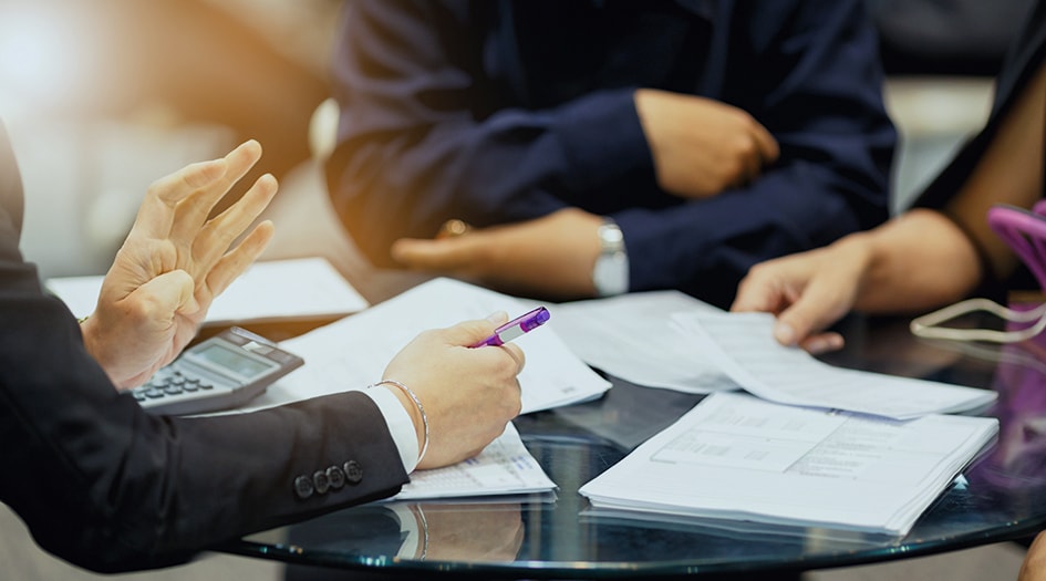 A close up on three individuals' hands as they sit around some papers illustrates the reasons why insurance companies cancel policies