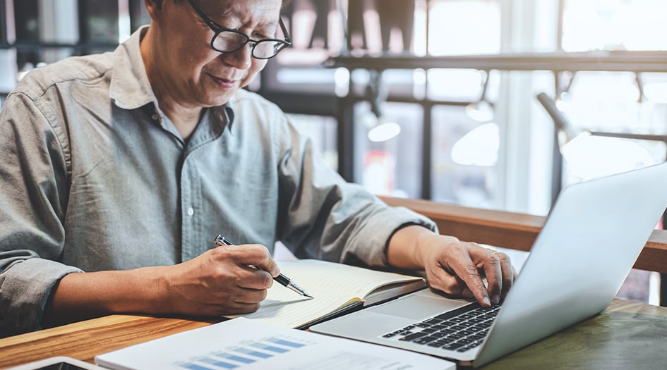 A man writes in a notebook and looks at his laptop, as he learns how a Hard Market impacts customers
