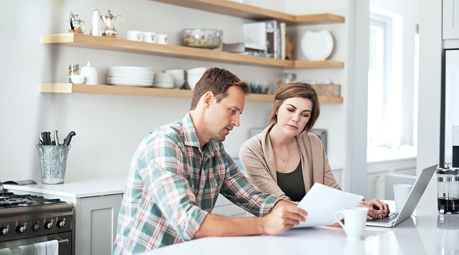 A couple reviews some paperwork with a laptop, as they avoid insurance seller scams and find a legitimate broker