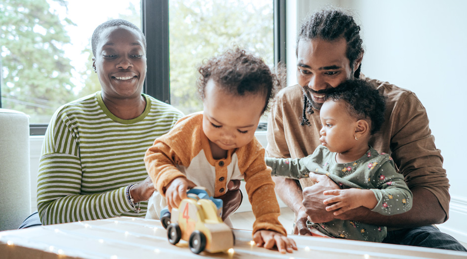 There are a variety of life stages that can affect home and car insurance needs, as shown by a couple playing with their two young children on the floor.