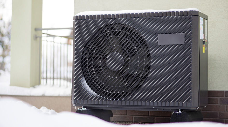A heat pump mounted on outside a home with snow on the ground shows how a heat pump works to heat and cool your home.