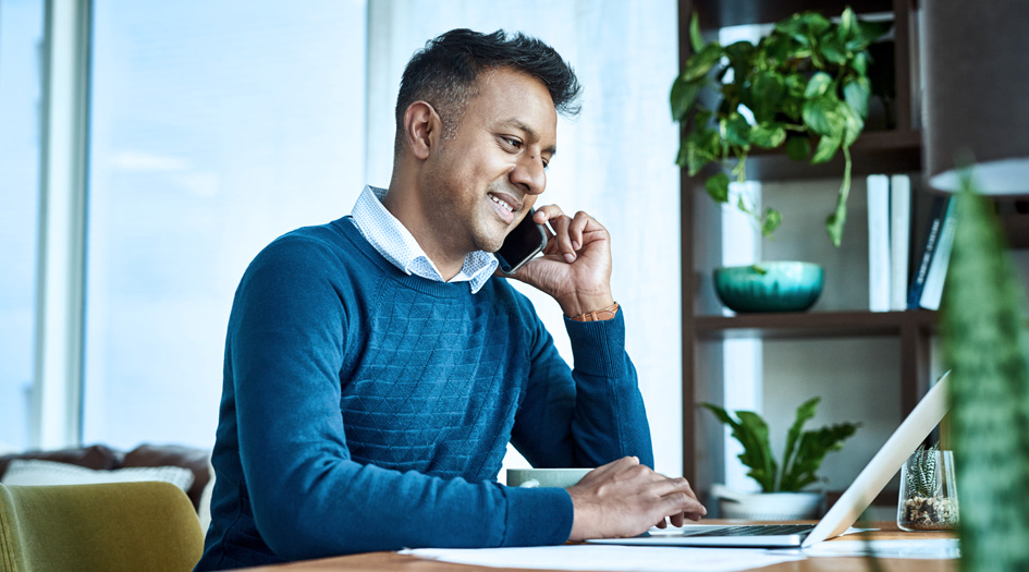A man sits at a desk talking on a mobile phone, as he saves money working with an insurance broker