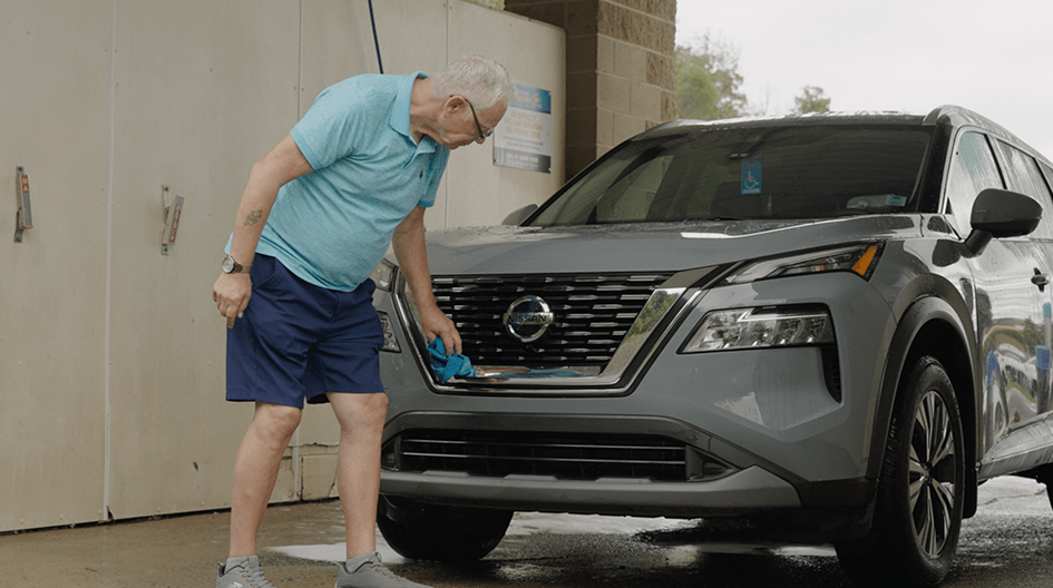Reed cleans off his SUV’s front bumper, showing how his insurance claim restored his new car after a fender bender.