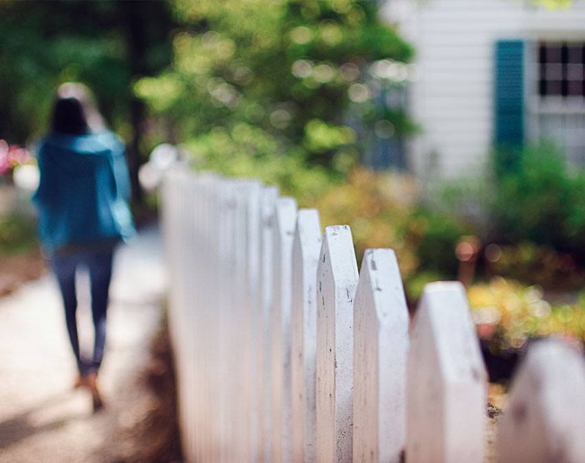 A woman walking next to a white picket fence