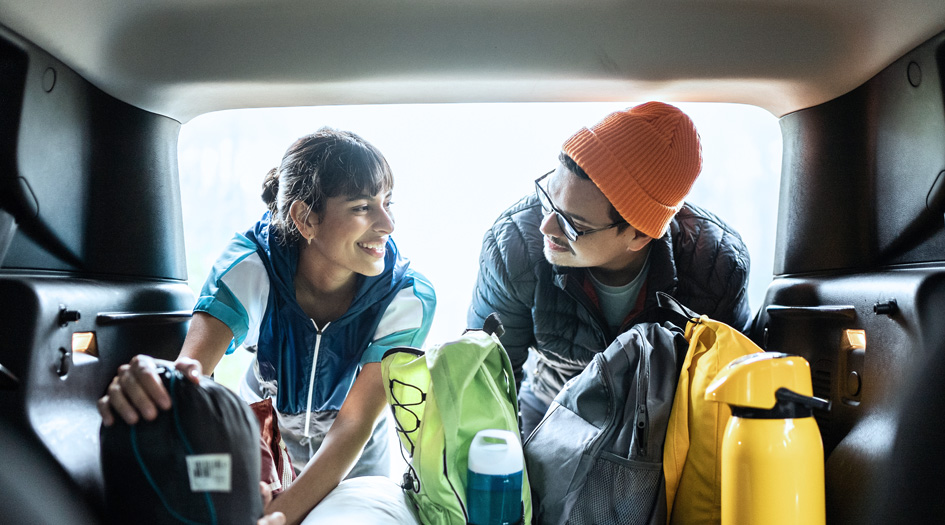 Un couple place leurs bagages dans leur voiture, illustrant ce que vous devriez avoir à bord lors d’une escapade routière.