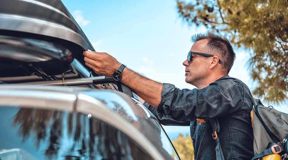 Un homme installe un porte-bagages sur le toit de sa voiture et se demande s’il aura une incidence sur son assurance auto.