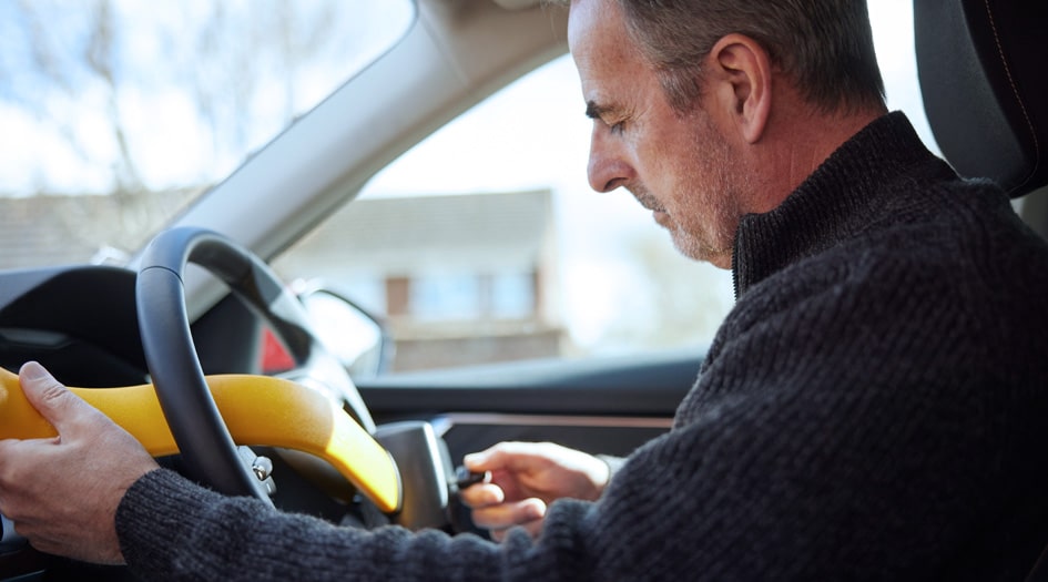 Un homme prévient le vol de son véhicule à l’aide d’un dispositif antivol jaune de blocage du volant d’après-vente.