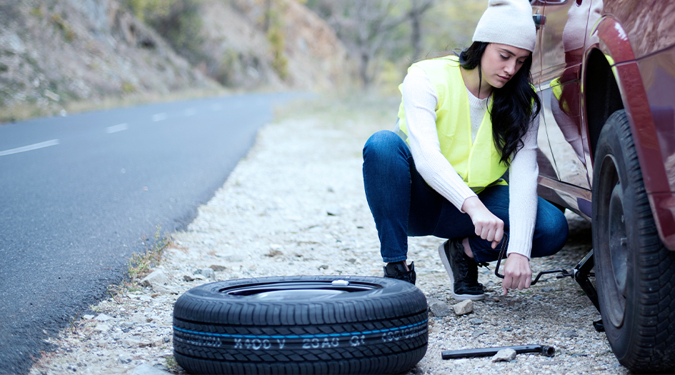 Une femme étend une veste au sol sous sa voiture afin d’illustrer comment changer une roue.