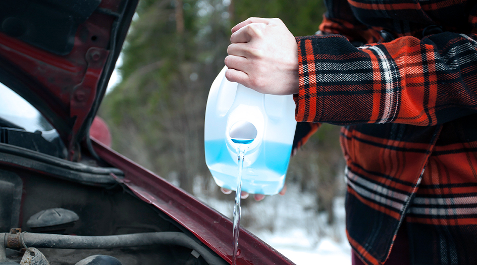 Un homme verse du lave-glace dans le réservoir de sa voiture, illustrant quel est le meilleur lave-glace à utiliser.