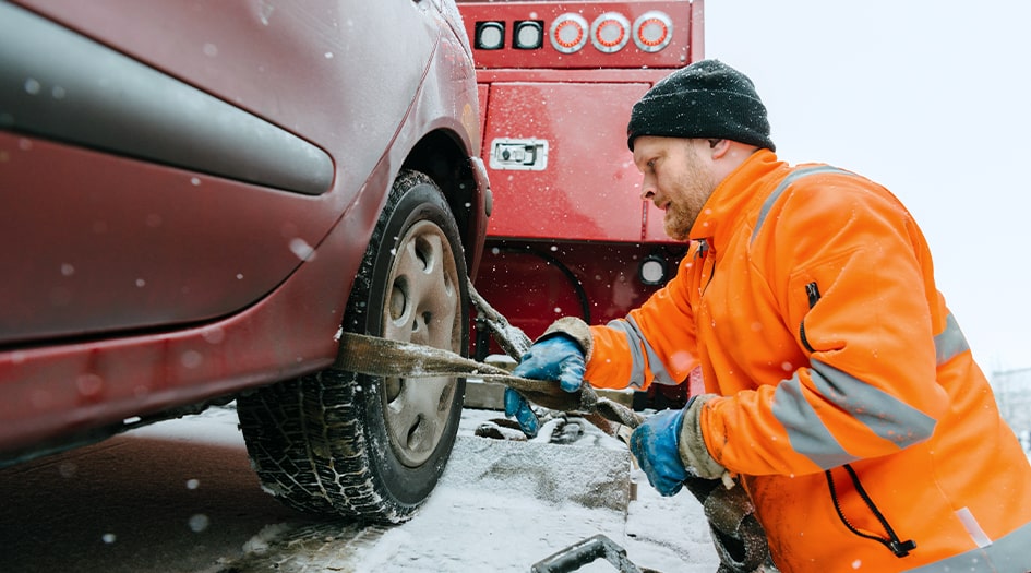 Un homme accroche les pneus de sa voiture à une remorqueuse, illustrant quoi faire avant que votre véhicule ne soit remorqué.
