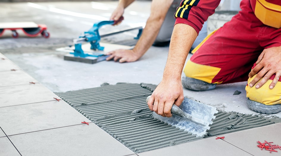 Deux personnes étalent du coulis en installant des tuiles sur un plancher, évitant les sept erreurs de rénovations.