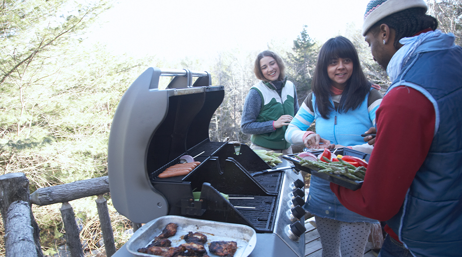 Trois personnes portent des manteaux devant un barbecue, illustrant comment faire des grillades l’hiver en toute sécurité.