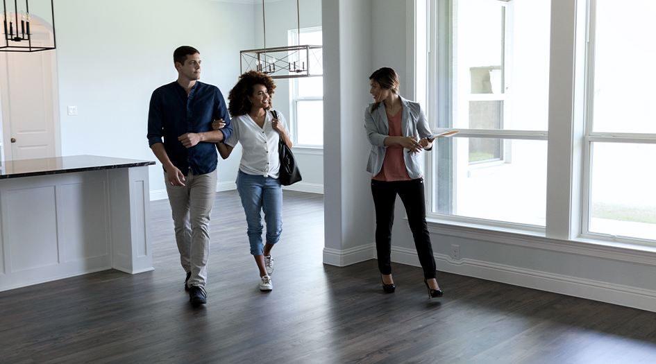Un couple en visite avec un courtier immobilier, qui explique qu’ils ont besoin d’une assurance habitation pour obtenir un prêt.