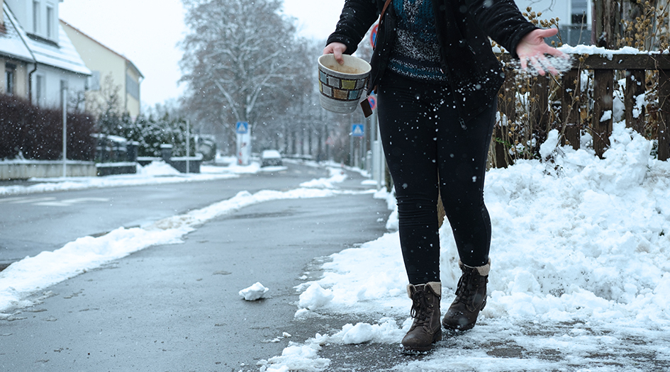 Une personne saupoudre du sel sur un trottoir glacé, démontrant comment garder vos trottoirs libres de glace durant l’hiver
