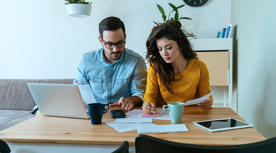 Un couple assis à la table avec un portable planifie des économies sur l’assurance en période d’incertitude économique