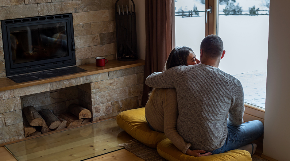 Un couple regarde la neige par la fenêtre, illustrant comment hiverniser un chalet pour en faire une résidence quatre saisons.