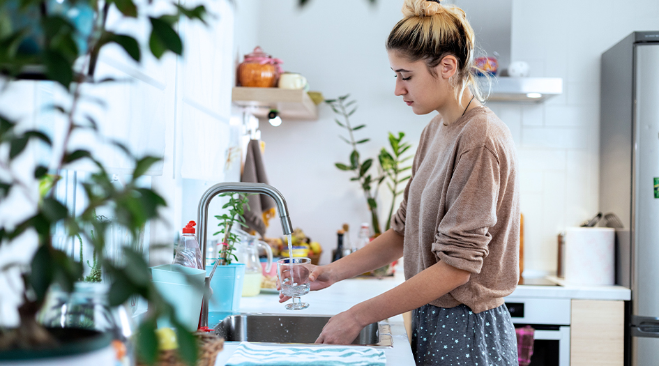Une femme remplit un verre au robinet de sa cuisine, illustrant comment prévenir les dégâts d’eau en tant que locataire.
