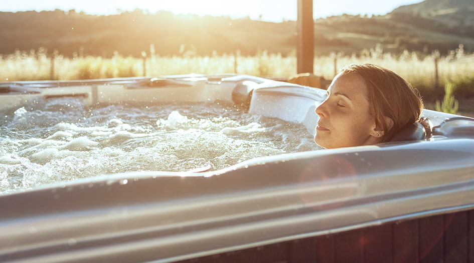 Une femme est assise dans un spa à l’extérieur, pour illustrer des raisons expliquant la hausse de votre facture d’eau.