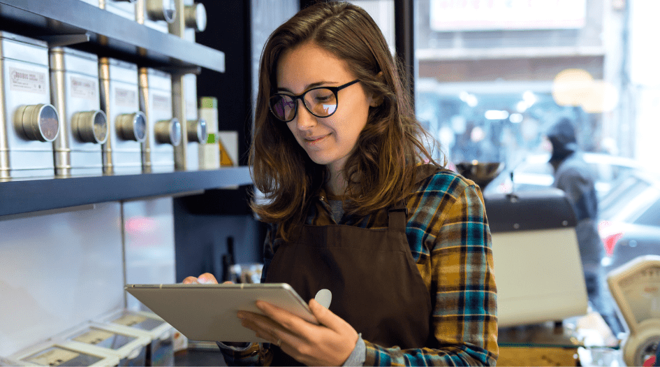 Une femme debout dans sa petite entreprise utilise sa tablette pour présenter une réclamation d’assurance biens des entreprises
