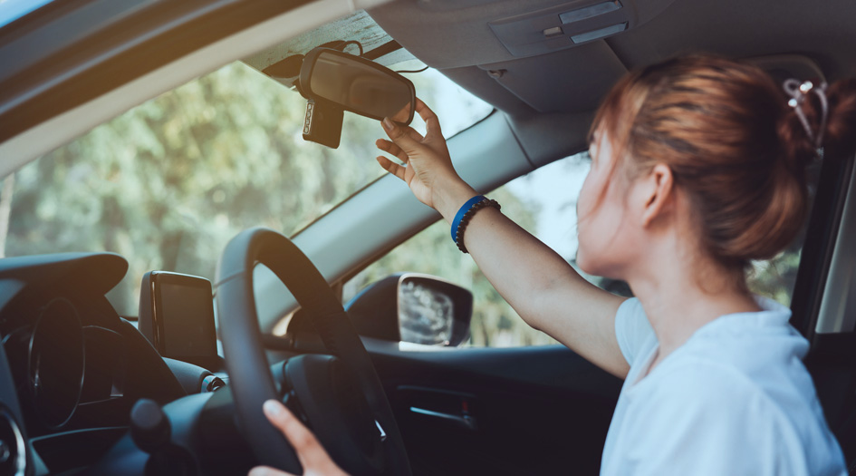 A woman checks her rearview mirror in her car, showing one way to protect yourself against carjacking